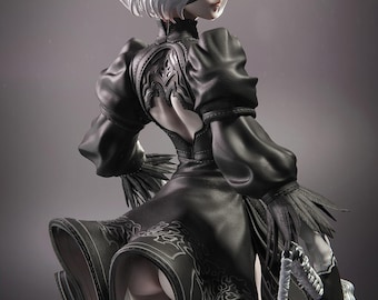 May include: A detailed figurine of a character with short white hair, a black blindfold, and a black outfit. The figure is holding a silver sword. The outfit has intricate patterns and a flowing skirt. The background is a solid gray.