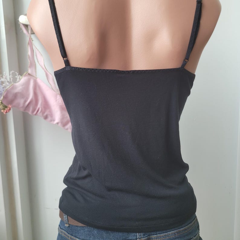Peut inclure: Camisole noire avec bretelles r&eacute;glables. Le haut a une encolure carr&eacute;e et une silhouette ajust&eacute;e. Les bretelles sont fines et le tissu semble &ecirc;tre un tricot doux. Le camisole est port&eacute; avec un jean bleu.