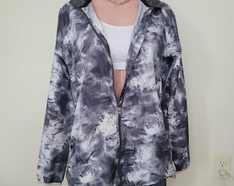 Op de afbeelding: Zwart-wit tie-dye print jasje met een volledige ritssluiting. De jas heeft een kraag en lange mouwen. Een witte top is eronder zichtbaar. De jas wordt op een mannequin gepresenteerd.