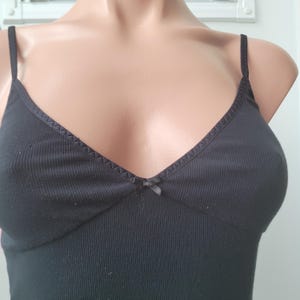 Peut inclure: D&eacute;bardeur noir avec fines bretelles et encolure en V. Le tissu c&ocirc;tel&eacute; pr&eacute;sente un petit n&oelig;ud au centre de la poitrine. Les bords de l'encolure sont orn&eacute;s d'une couture d&eacute;corative.