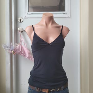 Peut inclure: Un caraco noir &agrave; fines bretelles et col en V est pr&eacute;sent&eacute; sur un mannequin. Le caraco a un petit n&oelig;ud au d&eacute;collet&eacute;. Le mannequin porte un jean bleu et une ceinture marron. Un soutien-gorge rose est accroch&eacute; &agrave; une poign&eacute;e de porte.