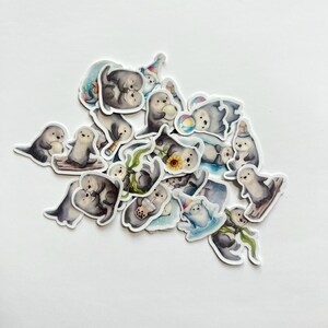May include: A collection of die-cut stickers featuring watercolor illustrations of sea otters in various poses. The otters are depicted holding items like boba tea, sunflowers, telescopes, and beach balls, or wearing party hats and scarves.