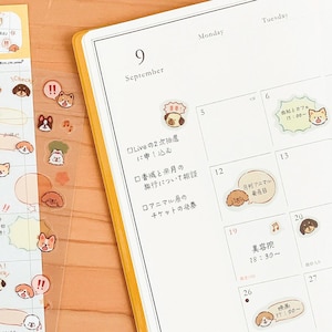 May include: A planner page for September with handwritten Japanese text and various small, colourful dog-themed stickers applied to the calendar grid. The stickers feature different dog breeds, speech bubbles, and musical notes, decorating the white paper.