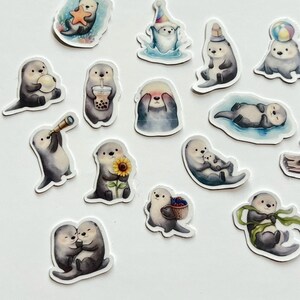 May include: A collection of die-cut stickers featuring illustrated sea otters in various poses, including holding a starfish, a sunflower, a boba tea, a telescope, a basket of berries, a ball, and wearing a party hat or wrapped in a green ribbon.