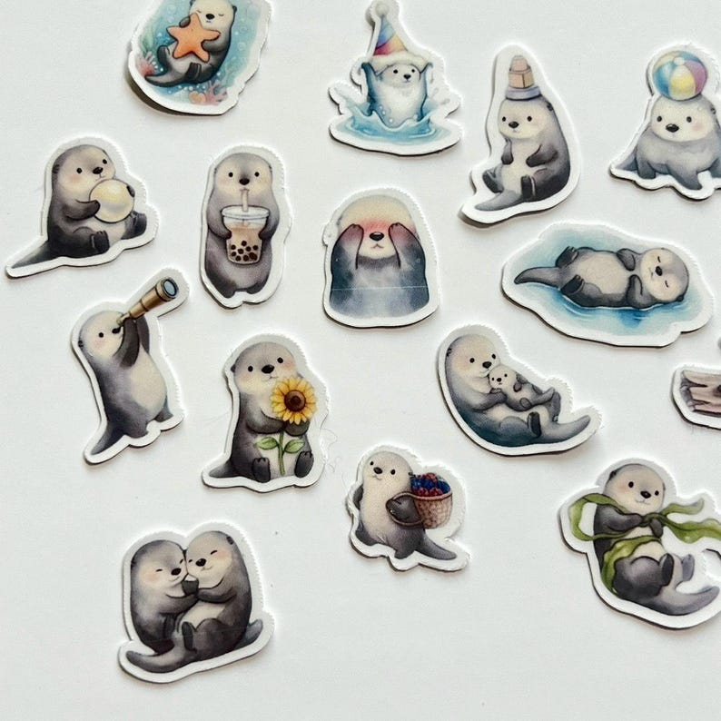 May include: A collection of die-cut stickers featuring illustrated sea otters in various poses, including holding a starfish, a sunflower, a boba tea, a telescope, a basket of berries, a ball, and wearing a party hat or wrapped in a green ribbon.