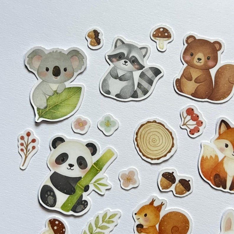May include: A collection of whimsical animal stickers featuring a koala, raccoon, bear, panda, fox, and squirrel. The stickers are in various shapes and sizes, with a white border. Additional stickers include mushrooms, flowers, acorns, and a tree slice.