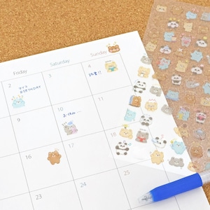 Könnte beinhalten: Eine weiße Kalenderseite mit Cartoon-Bären-Aufklebern und einem blauen Stift. Der Kalender hat Daten und Wochentage beschriftet. Einige Daten haben Aufkleber mit japanischem Text. Ein Bogen mit Aufklebern ist sichtbar.