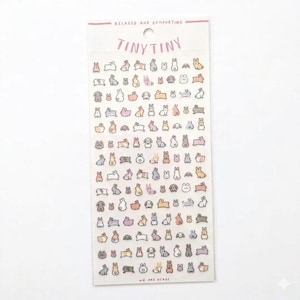 May include: A sheet of stickers featuring numerous small, cartoon rabbits in various poses and colors, including gray, pink, and brown. The stickers are arranged on a white background, with the words "TINY TINY" and "RELAXED AND COMFORTING" printed at the top. The text "WE ARE USAGI" is printed at the bottom.
