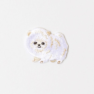 May include: Embroidered patch of a fluffy white Pomeranian dog with gold accents. The dog has black eyes and a small, smiling mouth. The patch is on a white background.