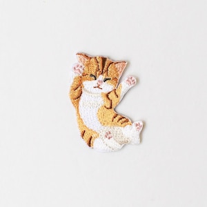May include: Embroidered patch featuring a relaxed orange and white tabby cat. The cat is lying down with one paw raised, and its eyes are closed. The patch has a detailed, stitched design on a white background.