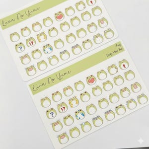 May include: Two sticker sheets with frog designs in light green and white. The frog stickers display various emotions. The text "Luna No Yume" is printed on the sheets. The text "Frog Daily Mood Kit" is also visible.