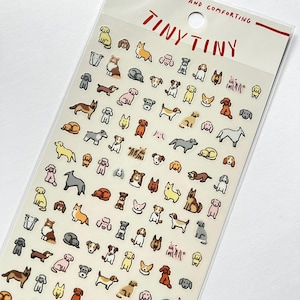 Peut inclure: Feuille d'autocollants transparente avec de nombreuses petites illustrations de chiens de différentes races et poses. La feuille porte les mots "TINY TINY" en rouge en haut. Les autocollants sont de différentes couleurs, dont le jaune, le marron, le gris et le rose.