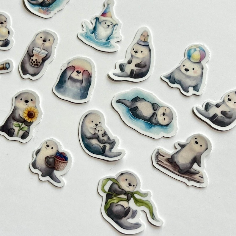 May include: A collection of die-cut stickers featuring various illustrations of sea otters. The otters are depicted in different poses, including holding a boba tea, a sunflower, a basket of berries, a beach ball, and wearing a party hat.