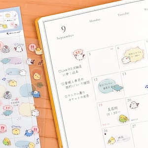 Peut inclure: Une page de calendrier mensuel pour septembre avec du texte manuscrit en japonais et divers petits autocollants d'oiseaux colorés appliqués sur la grille. Les autocollants représentent des oiseaux de dessin animé dans diverses poses.