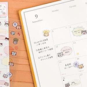 May include: A planner page for September with a yellow cover, featuring various small, transparent cat-themed stickers applied to the calendar grid. The stickers include illustrations of cats with different expressions, speech bubbles, and musical notes.