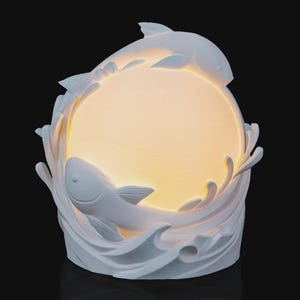 May include: A white, fish-themed lamp with a warm, glowing center. Two fish are sculpted on the lamp, appearing to leap through stylized waves. The lamp is a decorative accent piece.