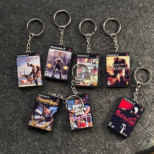 Peut inclure: Porte-clés avec des mini-boîtiers de jeux PlayStation 2. Les porte-clés présentent des titres de jeux tels que "God of War", "Grand Theft Auto: San Andreas" et "Shadow of the Colossus". Chaque porte-clés a un anneau et une chaîne argentés.