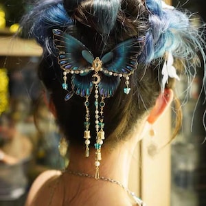 Puede incluir: Un accesorio para el cabello con una mariposa grande de color azul oscuro con alas transl&uacute;cidas, detalles en metal dorado, un peque&ntilde;o dije de media luna y tiras colgantes de perlas blancas, cuentas transparentes y peque&ntilde;os dijes dorados.