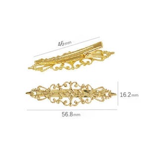 Puede incluir: Dos pinzas para el cabello de metal dorado con intrincados patrones de filigrana. Una pinza se muestra desde un &aacute;ngulo lateral midiendo 46 mm de largo, mientras que la otra se ve desde arriba midiendo 56,8 mm de largo y 16,2 mm de ancho.