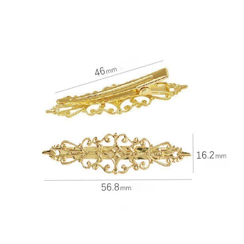 Puede incluir: Dos pinzas para el cabello de metal dorado con intrincados patrones de filigrana. Una pinza se muestra desde un &aacute;ngulo lateral midiendo 46 mm de largo, mientras que la otra se ve desde arriba midiendo 56,8 mm de largo y 16,2 mm de ancho.