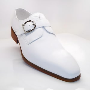 May include: A white leather shoe with a buckle closure. The shoe has a brown sole and heel. The buckle is silver-colored. The shoe is a formal style.