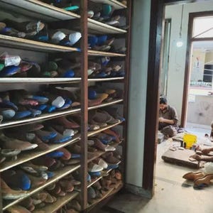 Peut inclure: Une grande &eacute;tag&egrave;re en bois remplie de nombreuses formes &agrave; chaussures de diff&eacute;rentes couleurs et formes. Les &eacute;tag&egrave;res sont organis&eacute;es en deux colonnes verticales, contenant une vaste collection de moules en bois pour la cordonnerie.