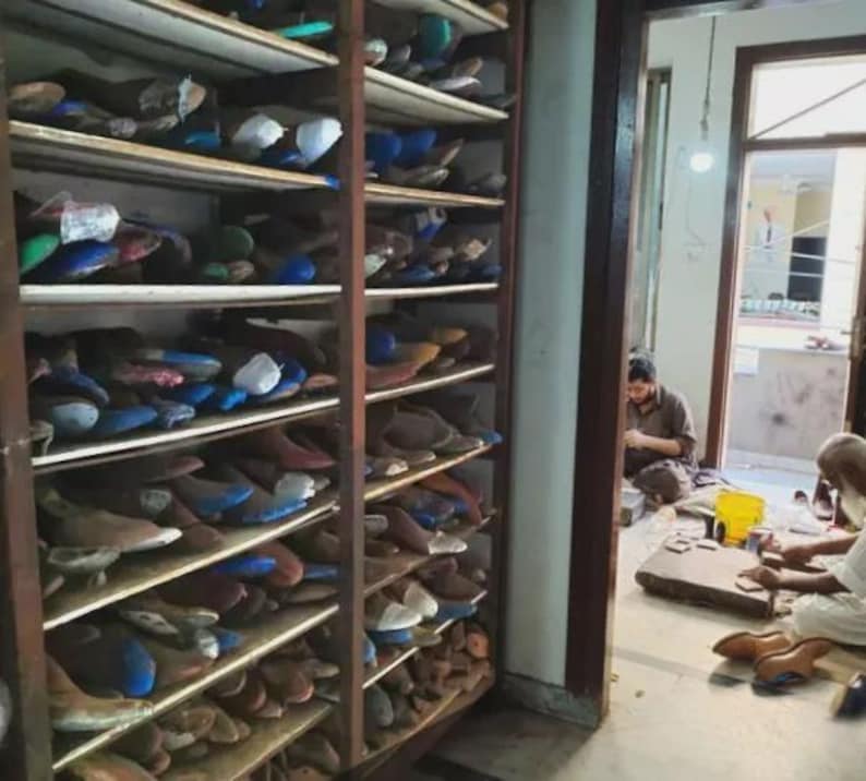 Peut inclure: Une grande &eacute;tag&egrave;re en bois remplie de nombreuses formes &agrave; chaussures de diff&eacute;rentes couleurs et formes. Les &eacute;tag&egrave;res sont organis&eacute;es en deux colonnes verticales, contenant une vaste collection de moules en bois pour la cordonnerie.