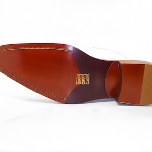 May include: A close-up of the sole of a dress shoe, showcasing its construction. The sole is a rich brown color with a stitched perimeter and a heel. The heel is a lighter shade of brown with a textured pattern.