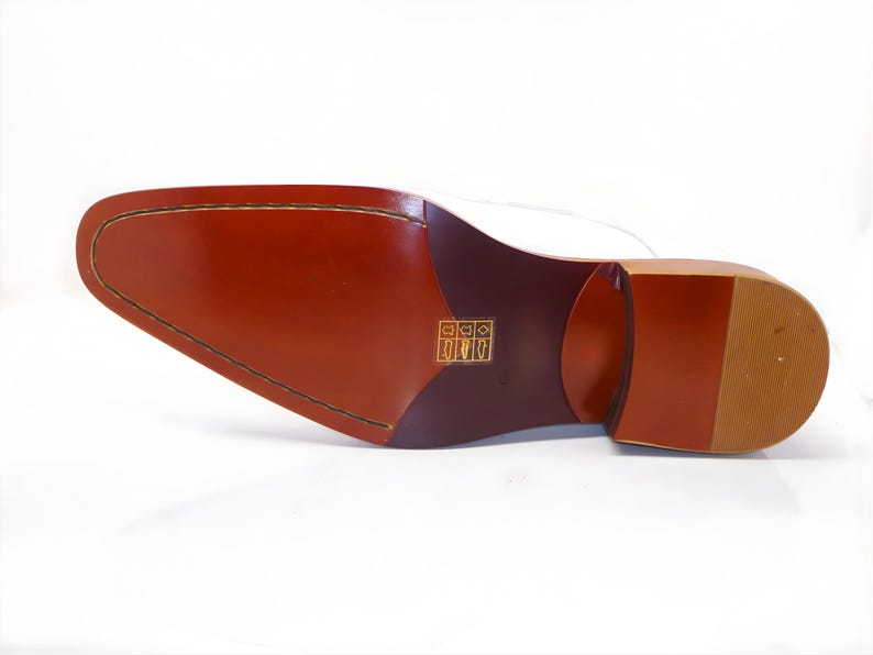 May include: A close-up of the sole of a dress shoe, showcasing its construction. The sole is a rich brown color with a stitched perimeter and a heel. The heel is a lighter shade of brown with a textured pattern.
