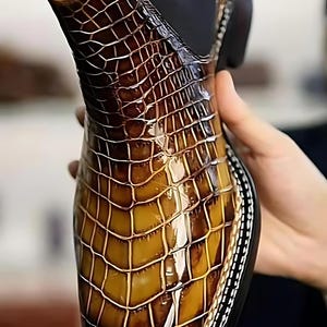 Handmade brown crocodile pattern leather Chelsea boots for men with glossy finish and elastic side panels, slip-on dress boots held in hand showing detailed texture.