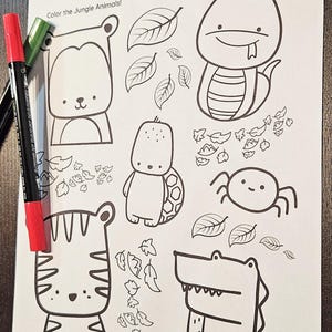 Può includere: Una pagina da colorare in bianco e nero intitolata "Animali della giungla" con contorni di un orso, un serpente, una tartaruga, un ragno, una tigre e un alligatore. La pagina include foglie e il testo "Colora gli animali della giungla!" Sono visibili pennarelli rossi e verdi.