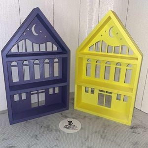 May include: Two wooden house-shaped shelves, one in a deep purple and the other in bright yellow. Each shelf has a gable roof with a crescent moon and star cutouts. The shelves have multiple window cutouts and a small shelf inside.