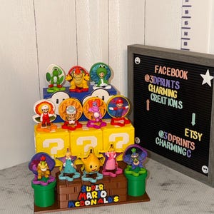 May include: A Super Mario display featuring various character figurines. The display includes yellow question mark blocks, green pipes, and a sign that reads "Super Mario McDonalds". The sign also includes Etsy and Facebook information.