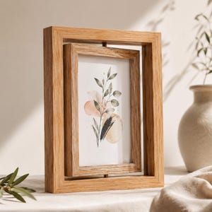 Op de afbeelding: Een dubbelzijdig houten fotolijstje met een lichtbruine afwerking. Het bevat een aquarelprint van botanische elementen in perzik, beige en zwart. Het frame kan draaien en biedt twee weergaveopties. Het frame is van hout.