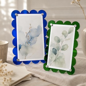 May include: Two rectangular picture frames with scalloped edges. One frame is translucent blue and the other is translucent green. Both frames feature four silver-toned metal fasteners at the corners to hold a white insert with botanical art.