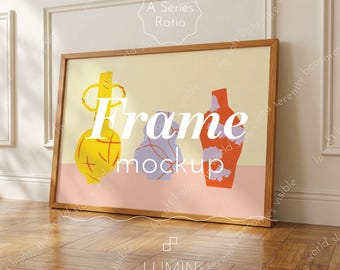 May include: Wooden framed art print featuring a minimalist design of three abstract vases in yellow, purple, and orange against a light background. The words "Frame mockup" are displayed on the artwork. The frame is leaning against a wall.