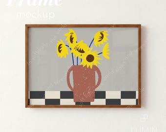 May include: A rectangular wooden frame containing a print of a terracotta-colored vase with two handles holding yellow sunflowers. The vase sits on a black and white checkered surface against a solid gray background. The text Frame mockup is visible.