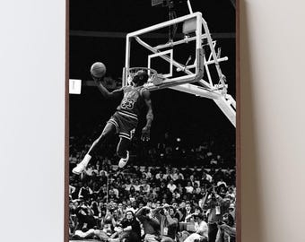May include: Black and white framed print of a basketball player mid-air, about to dunk the ball. The player wears a jersey with the number 23. The background shows a crowd of spectators in a stadium.