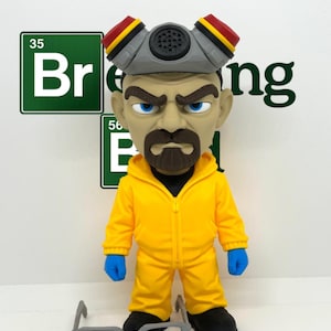 Könnte beinhalten: Eine stilisierte Figur eines Mannes mit Ziegenbart, bekleidet mit einem gelben Kapuzenoverall, blauen Handschuhen und schwarzen Schuhen. Die Figur trägt eine graue Atemschutzmaske mit roten und gelben Akzenten auf dem Kopf. Eine graue Brille liegt davor.