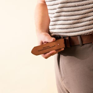 Puede incluir: Un cintur&oacute;n de cuero marr&oacute;n con hebilla plateada. El cintur&oacute;n se sostiene, mostrando el texto grabado "Don't worry, I'm always close to your waist". Un accesorio cl&aacute;sico.
