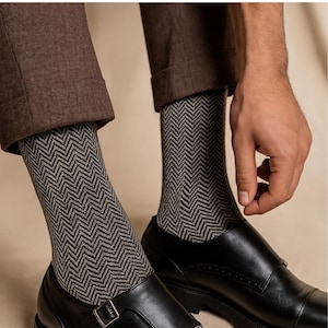K&ouml;nnte beinhalten: Nahaufnahme von gemusterten Socken mit einem schwarz-grauen Fischgr&auml;tmuster. Die Socken werden mit schwarzen Lederschuhen und einer braunen Hose getragen. Das Bild zeigt die Socken und Schuhe im Detail.