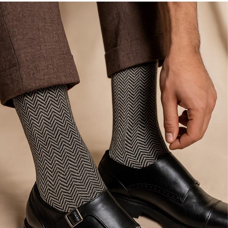 K&ouml;nnte beinhalten: Nahaufnahme von gemusterten Socken mit einem schwarz-grauen Fischgr&auml;tmuster. Die Socken werden mit schwarzen Lederschuhen und einer braunen Hose getragen. Das Bild zeigt die Socken und Schuhe im Detail.