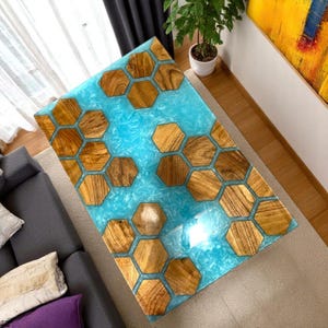 Könnte beinhalten: Rechteckiger Couchtisch mit einzigartigem Design. Er hat eine hellblaue Harzmitte mit eingelegten sechseckigen Holzformen. Das Holz hat eine natürliche Maserung, und der Tisch ist von einem Holzrahmen umgeben. Misst ca. 120 cm x 60 cm.