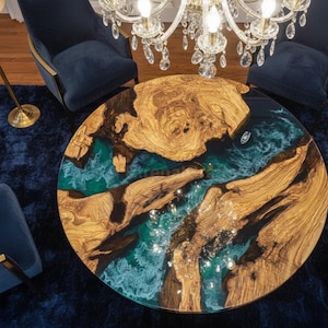 Puede incluir: Una mesa de centro redonda con un diseño único. La mesa presenta una superficie de madera con un patrón de vetas natural, combinada con resina epoxi de color turquesa. La mesa está rodeada de sillas azules y una alfombra azul.