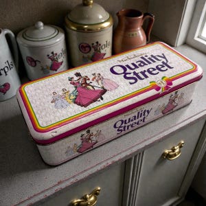 May include: A rectangular white metal tin featuring the Mackintosh's Quality Street logo in purple text. The lid and sides are decorated with colourful illustrations of figures in historical attire, accented by a rainbow-coloured border design.