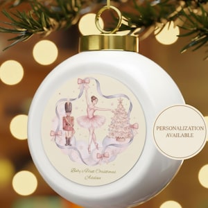 Könnte beinhalten: Weiße Weihnachtskugel mit goldener Kappe, die an einem Weihnachtsbaum hängt. Der Schmuck zeigt ein Design mit Ballerina, Nussknacker und Weihnachtsbaum in zarten Rosa- und Blautönen. Auf dem Ornament steht "Baby's First Christmas" und "Personalisierung verfügbar."