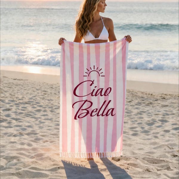 Ciao Bella lemon stripe beach towel in pink and white, held by a woman at the ocean