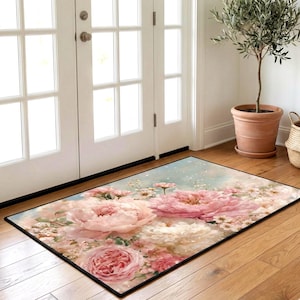 Puede incluir: Alfombra rectangular floral con grandes peonías y rosas rosas y blancas sobre un fondo azul claro. La alfombra tiene un borde negro y está colocada sobre un suelo de madera, adecuada para una entrada.