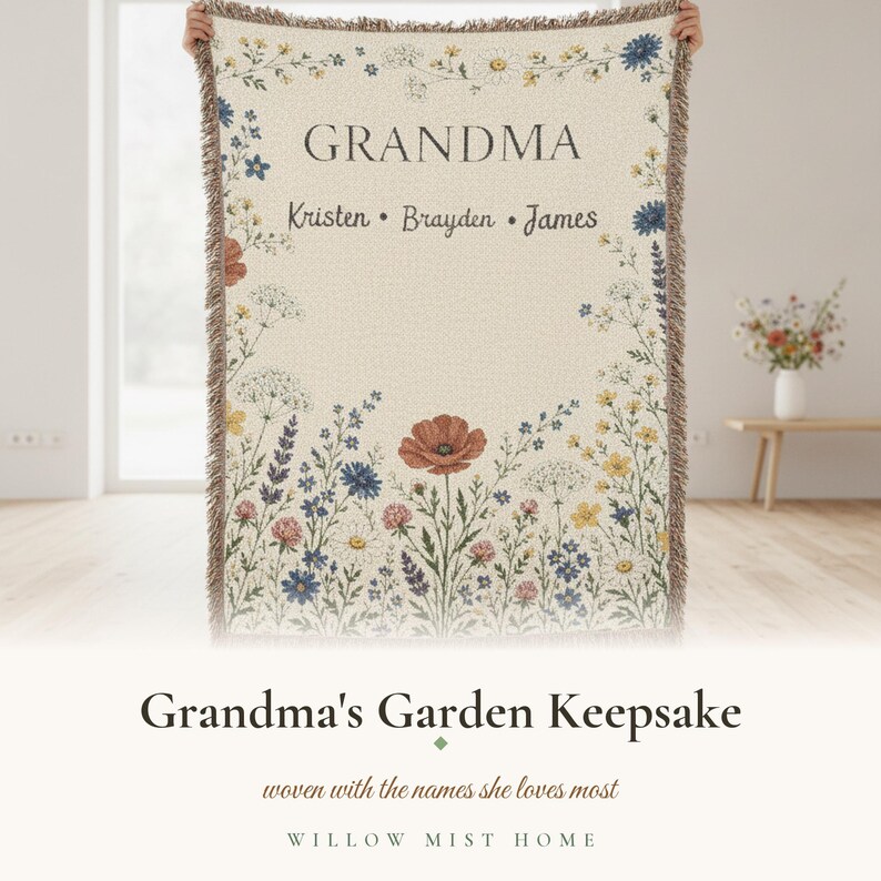 May include: A cream-colored woven throw blanket featuring a floral border of wildflowers in shades of red, blue, and yellow. The text GRANDMA is printed at the top, followed by the names Kristen, Brayden, and James in a dark serif font.
