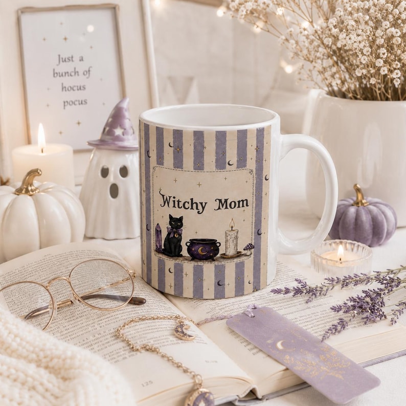 May include: A white ceramic mug featuring a vertical lavender and cream striped pattern. The center design displays a black cat, a purple cauldron, a candle, and the text Witchy Mom. The mug is decorated with small stars and crescent moon icons.